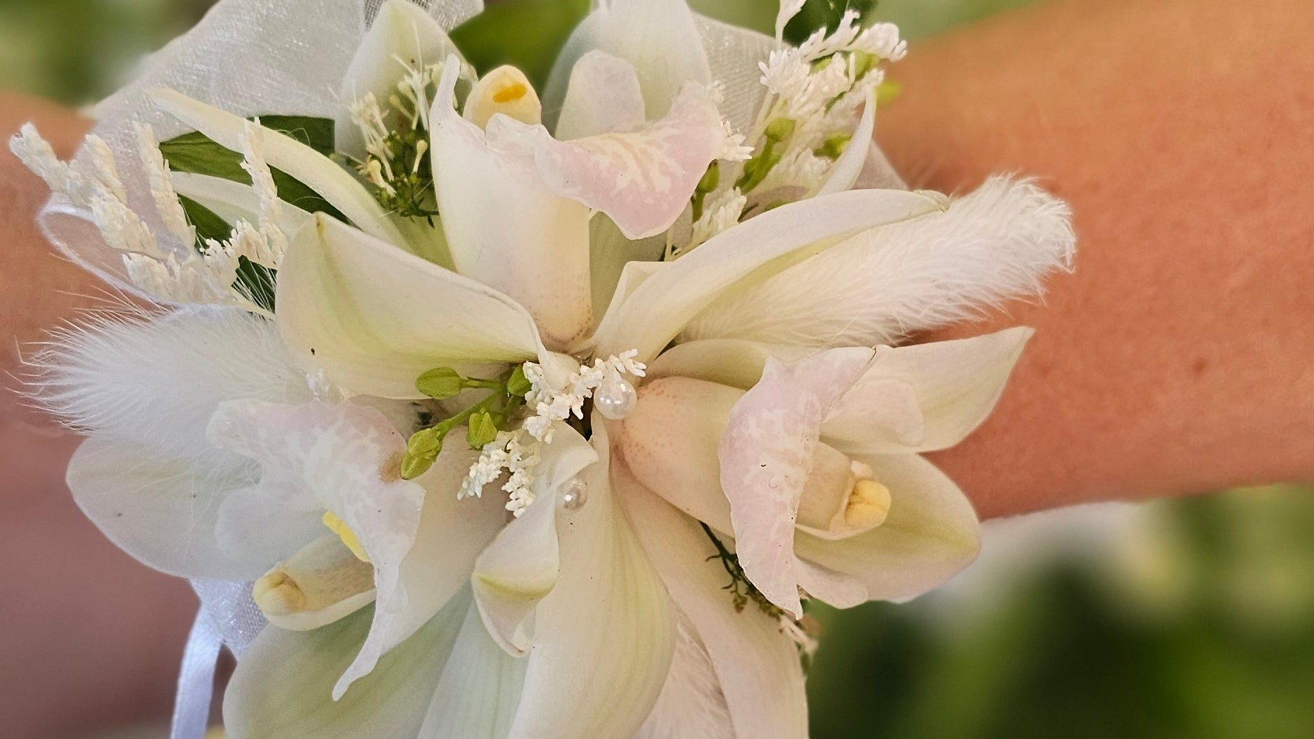 Close-up of a wrist wearing a white floral corsage with a blurred background